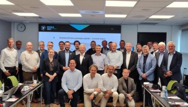 Group of business professionals posing for a photo in a conference room with a large screen behind them.