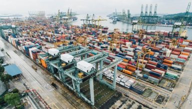 Aerial view of a busy shipping port with multicolored shipping containers and towering gantry cranes by the water