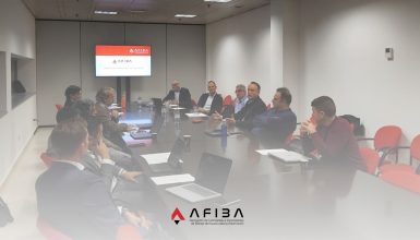Group of professionals seated around a long conference table with laptops and papers, in a corporate meeting room (AFIBA branding visible).